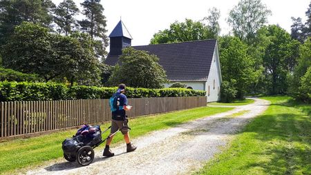 Ein Pilgerer mit Ziehwagen auf einem Weg zu einem Haus.