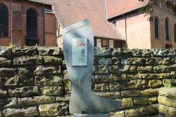 Übergroßer Schusterstiefel mit Beschreibungstafel vor einer Mauer in Wittingen.