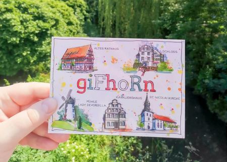 Eine Hand hält eine Postkarte mit gezeichneten Gifhorn-Motiven.