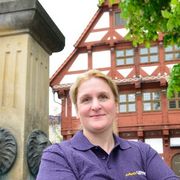 Daniela Reiter Frau mit verschränkten Armen vor einem Brunnen und einem Fachwerkhaus.