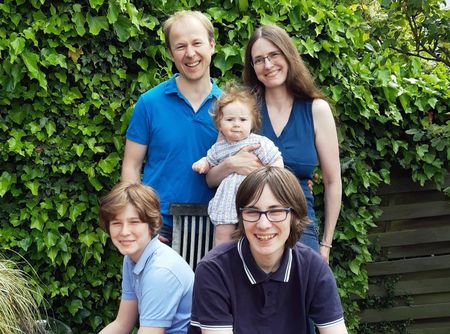 Ein Mann, eine Frau, zwei Jungen und ein Baby vor einer grünen Pflanze.