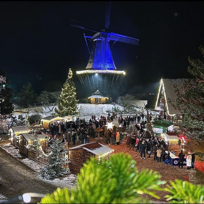 Beleuchteter Dorfplatz mit Buden im Internationalen Mühlenmuseum mit beleuchteter Mühle. 
