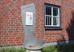 Übergroßer Schusterstiefel mit Beschreibungstafel vor einem Gebäude in Wittingen.